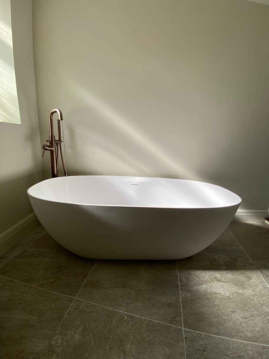 Bath & brass details Freestanding white bath beside a window with stone-effect floor tiles