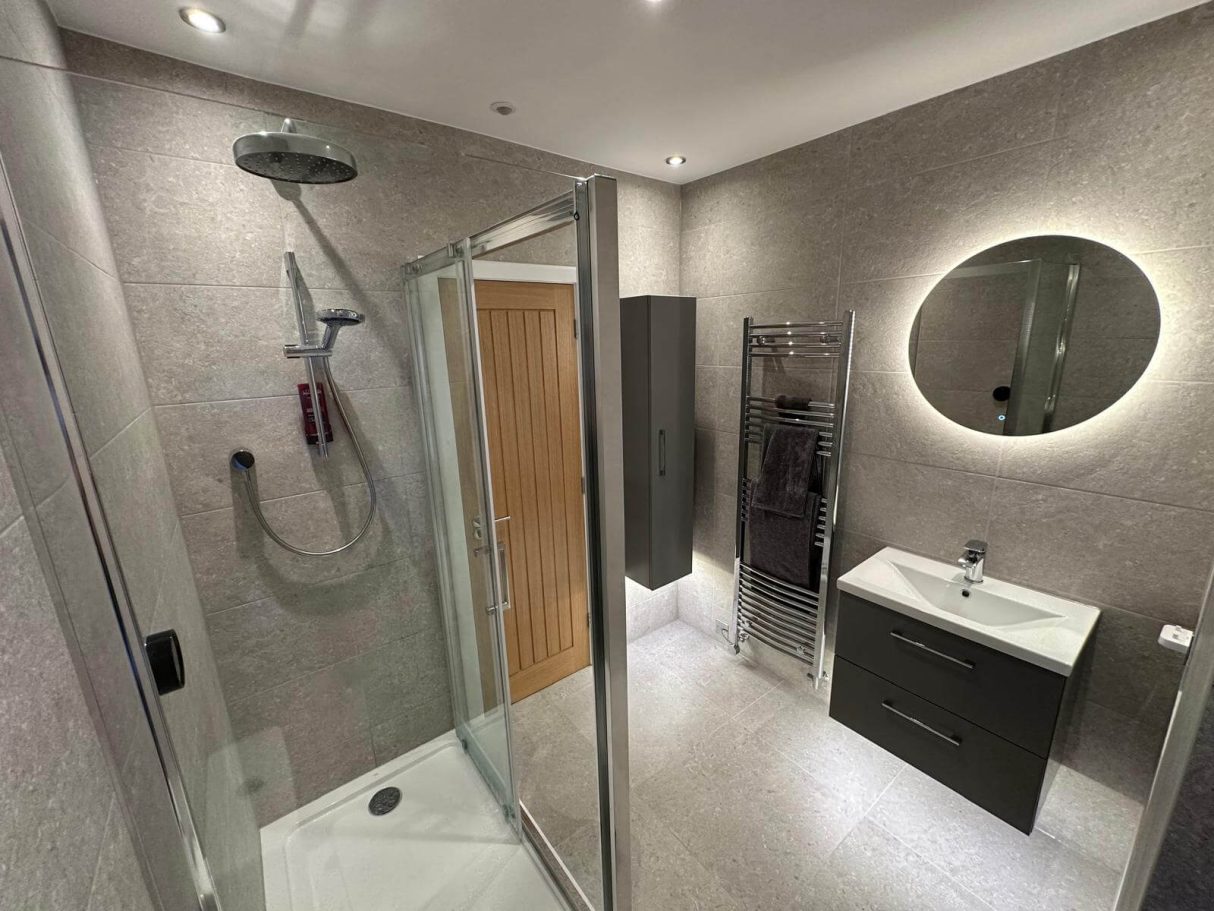 Brislington bathroom renovation Glass shower enclosure beside a grey tiled vanity and illuminated mirror